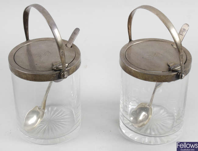 A pair of glass preserve pots with silver mounted covers.