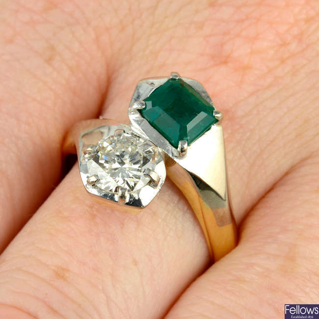 An emerald and brilliant-cut diamond two-stone crossover ring.