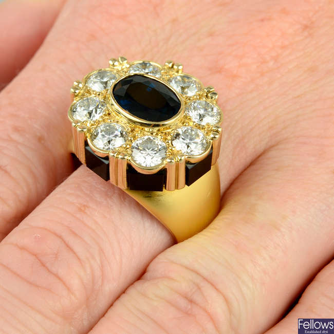 An 18ct gold sapphire and brilliant-cut diamond cluster ring, with onyx panel gallery.