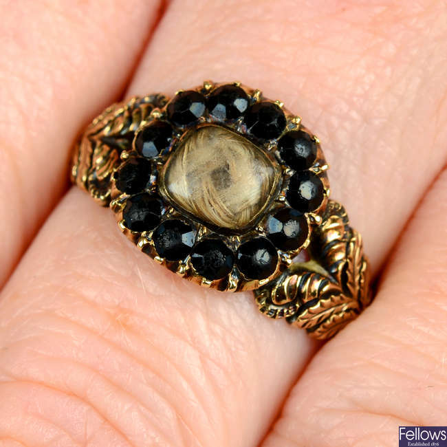 A Georgian gold black garnet mourning ring, with hairwork panel and foliate shoulders.
