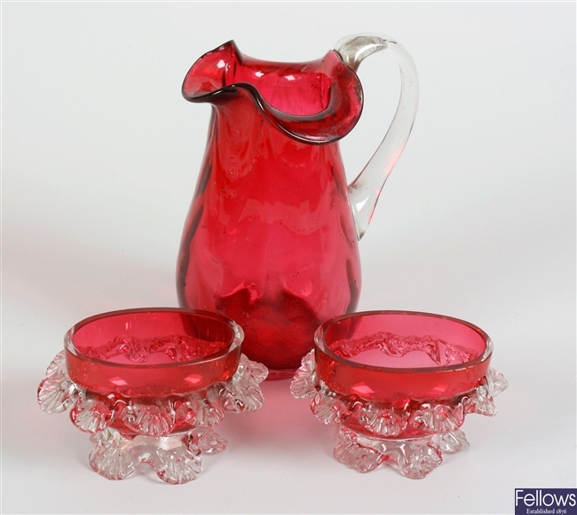 A cranberry glass jug with frilled collar and a pair of similar salts