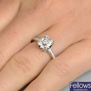 A cushion-shape diamond single-stone ring, with brilliant-cut diamond line shoulders.
