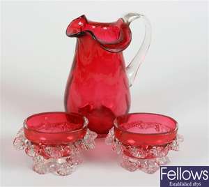 A cranberry glass jug with frilled collar and a pair of similar salts