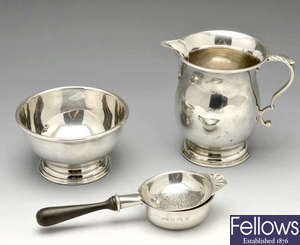 A modern silver tea strainer, milk jug and sugar bowl.