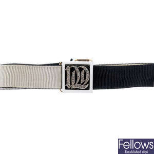 An early 20th century fabric bracelet with diamond and enamel initial panel.